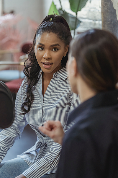 African American woman in blue and white stripped shirt speaking to a Caucasian woman