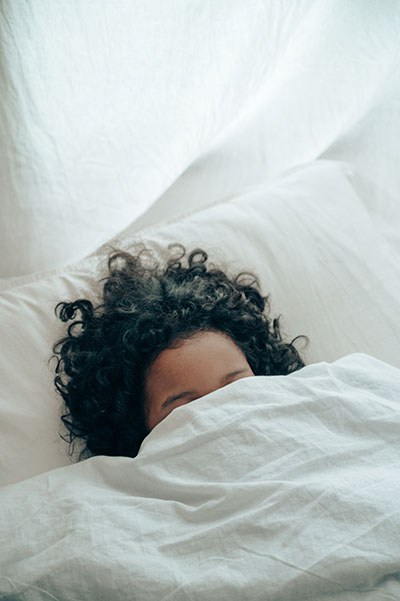 woman in bed hiding under the coveres