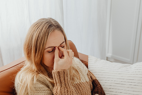 woman pinching bridge of nose, in sinus pain